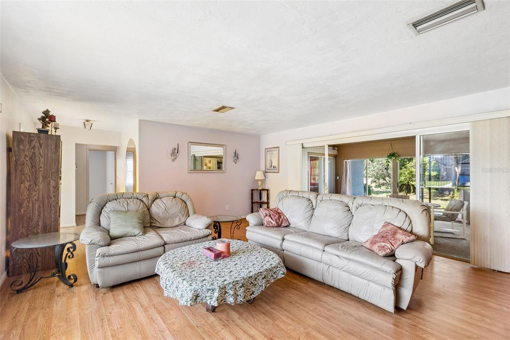 A living room features light wood flooring, two leather sofas, and a sliding glass door — 2059 WATERFALL DRIVE, SPRING HILL, FL