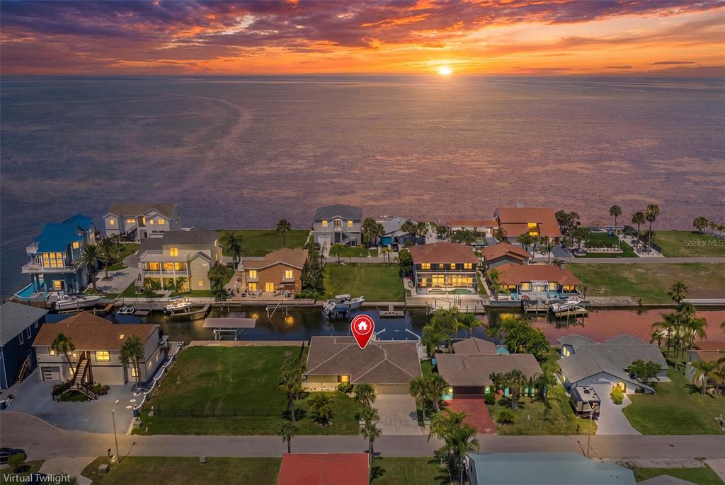 An aerial view shows a waterfront house with a canal and sunset over the ocean — 13525 CLAUDIA DRIVE, HUDSON, FL