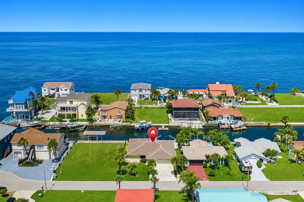 An aerial view shows a waterfront house with a canal and the ocean beyond — 13525 CLAUDIA DRIVE, HUDSON, FL