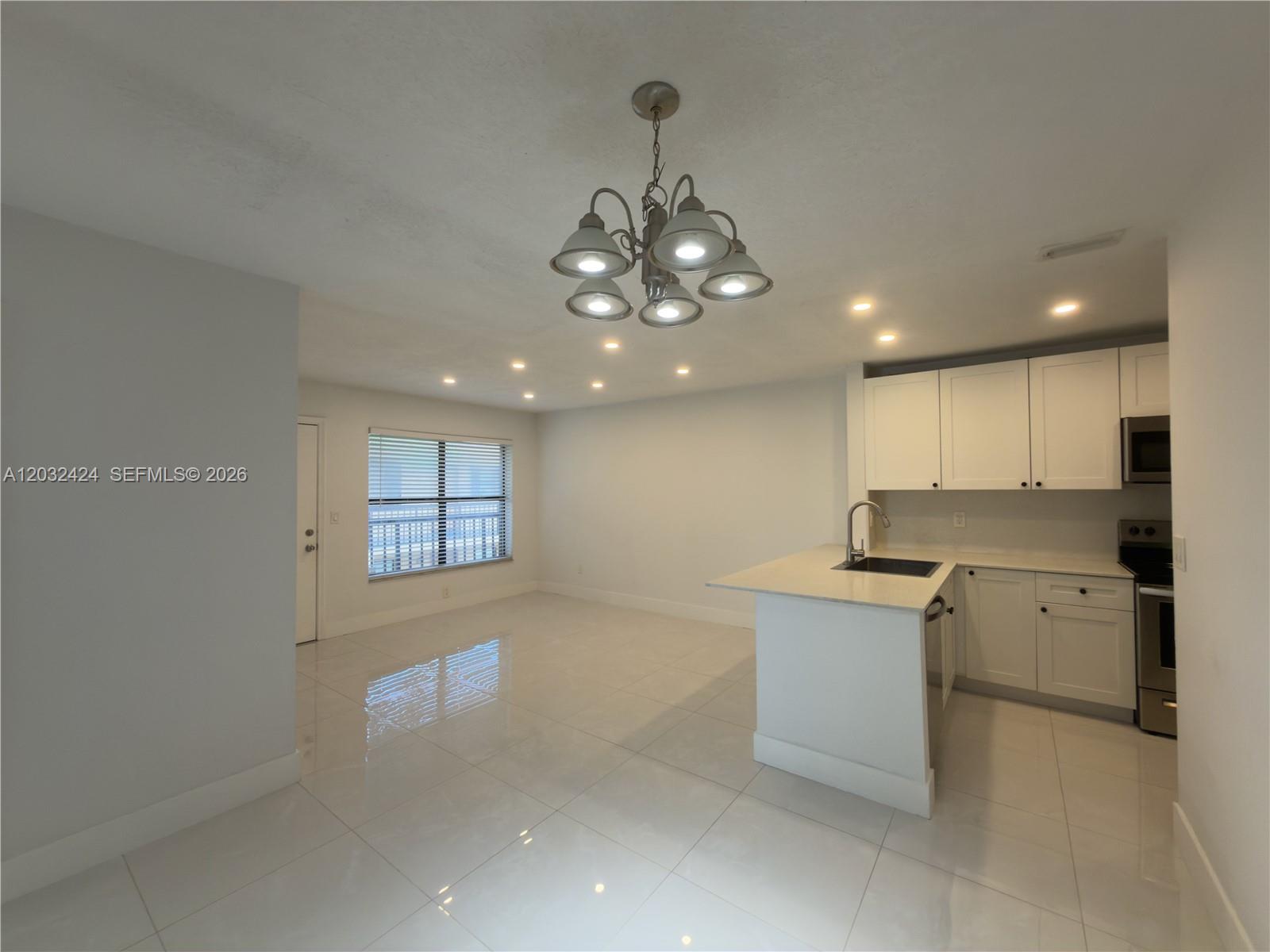 A kitchen with white cabinets and a center island opens into a tiled living area — 2500 W 67th Pl # 26, Hialeah FL 33016, HIALEAH, FL