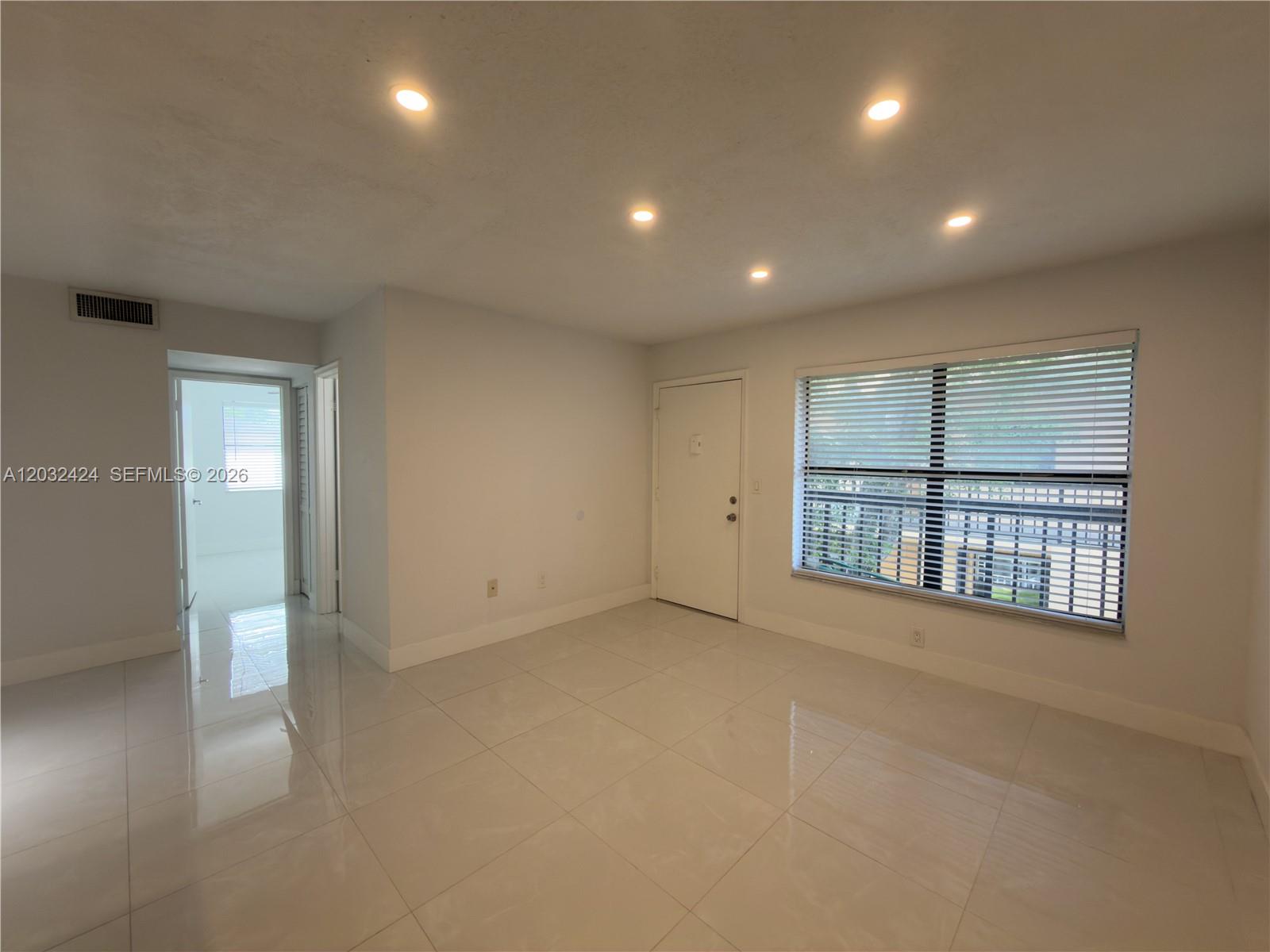 A bright, empty room features white tile floors, recessed lighting, and a large window — 2500 W 67th Pl # 26, Hialeah FL 33016, HIALEAH, FL