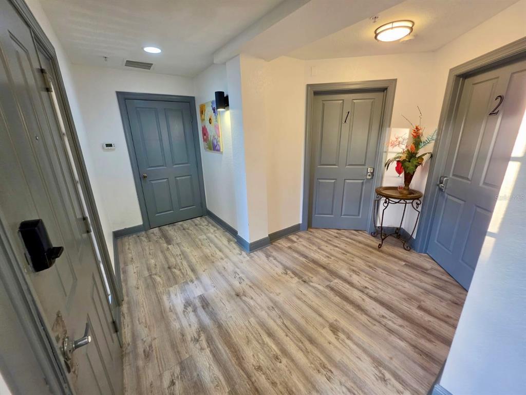 A hallway with wood-look flooring features three gray doors and a small decorative table — 7510 SEVEN EAGLES WAY UNIT 7510, REUNION, FL