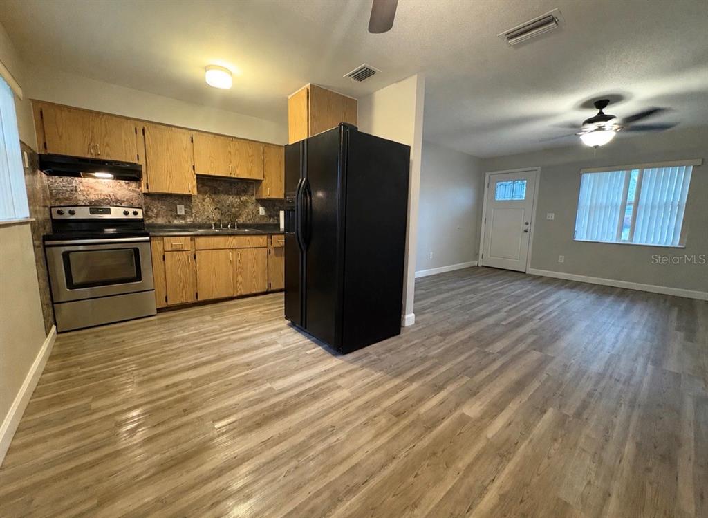 A kitchen with wood cabinets and stainless appliances opens into a living area with flooring — 2240 WHITE SANDS DRIVE, TITUSVILLE, FL