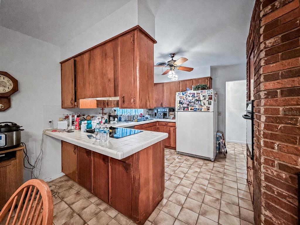 A kitchen features wood cabinets, tile countertops, a white refrigerator, and a brick wall — 2340 DERBYSHIRE ROAD, MAITLAND, FL