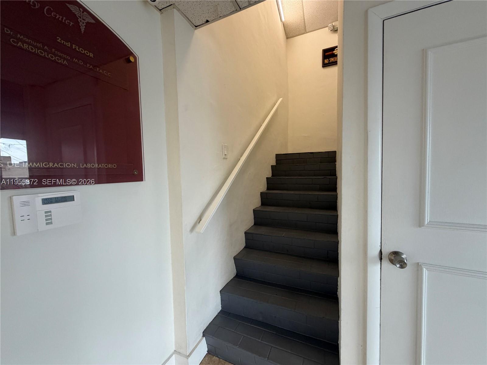 A staircase with dark gray steps leads upward between a white wall and a white door — 600 NW 35th Ave # 201, Miami FL 33125, MIAMI, FL