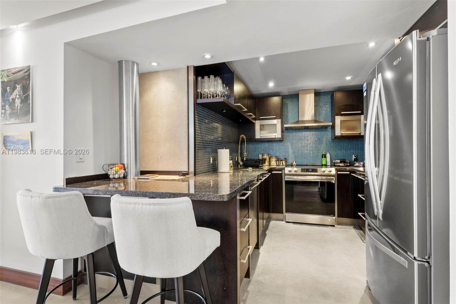 A modern kitchen features dark cabinetry, granite countertops, stainless steel appliances, and blue tile backsplashes — 2500 Parkview Dr # 2319, Hallandale Beach FL 33009, HALLANDALE BEACH, FL