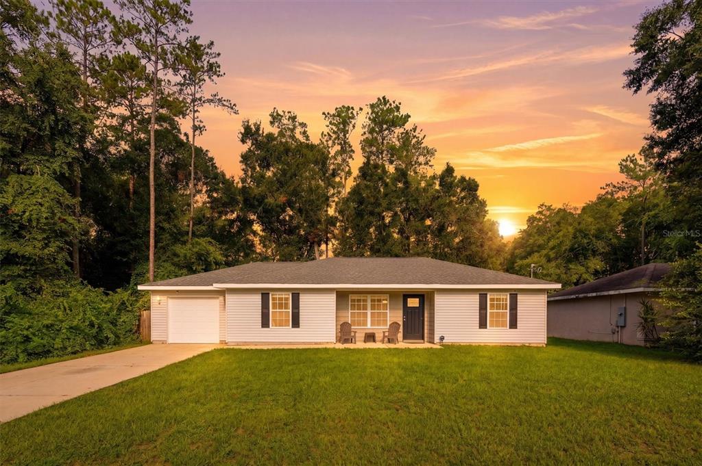A single-story house with white siding, a garage, and a lawn at sunset — 4918 NW 61ST COURT, OCALA, FL