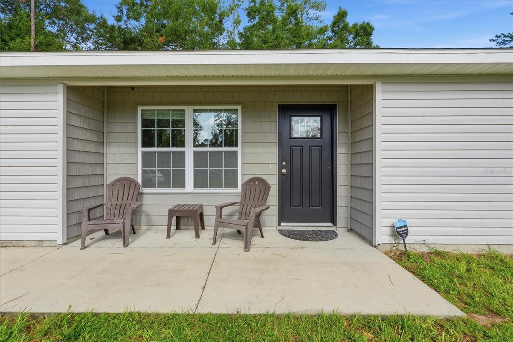 A concrete porch features two brown chairs, a small table, and a black front door — 4918 NW 61ST COURT, OCALA, FL