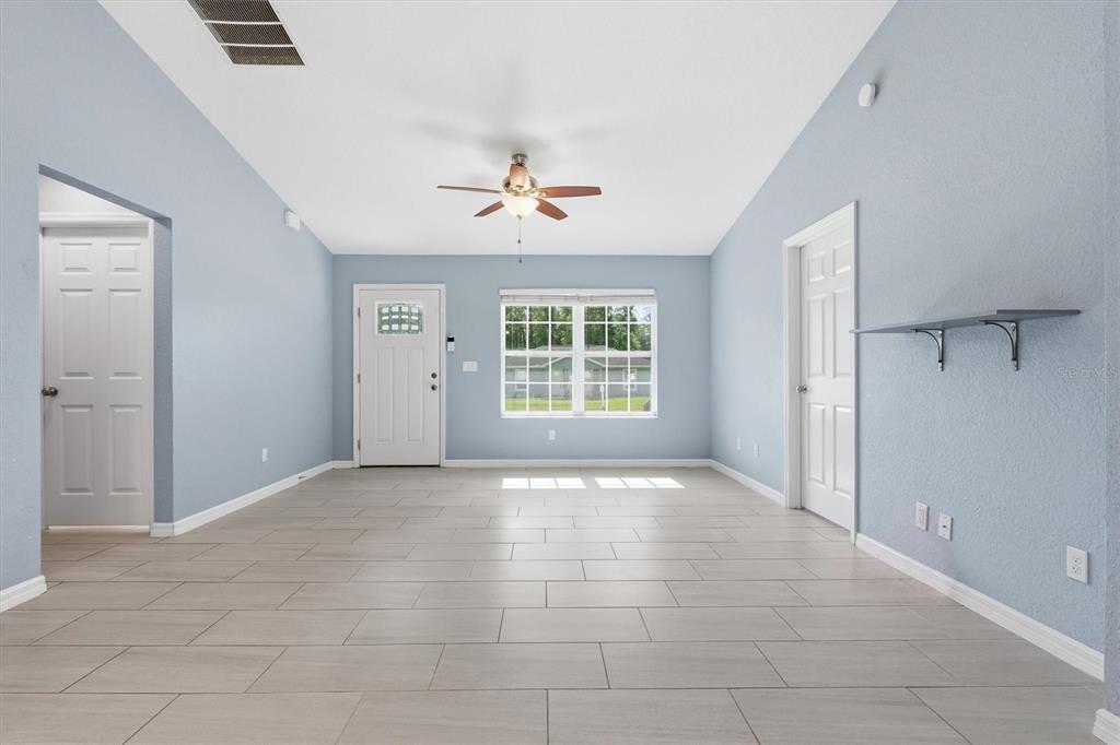 A bright living room features light blue walls, tile flooring, a ceiling fan, and doors — 4918 NW 61ST COURT, OCALA, FL
