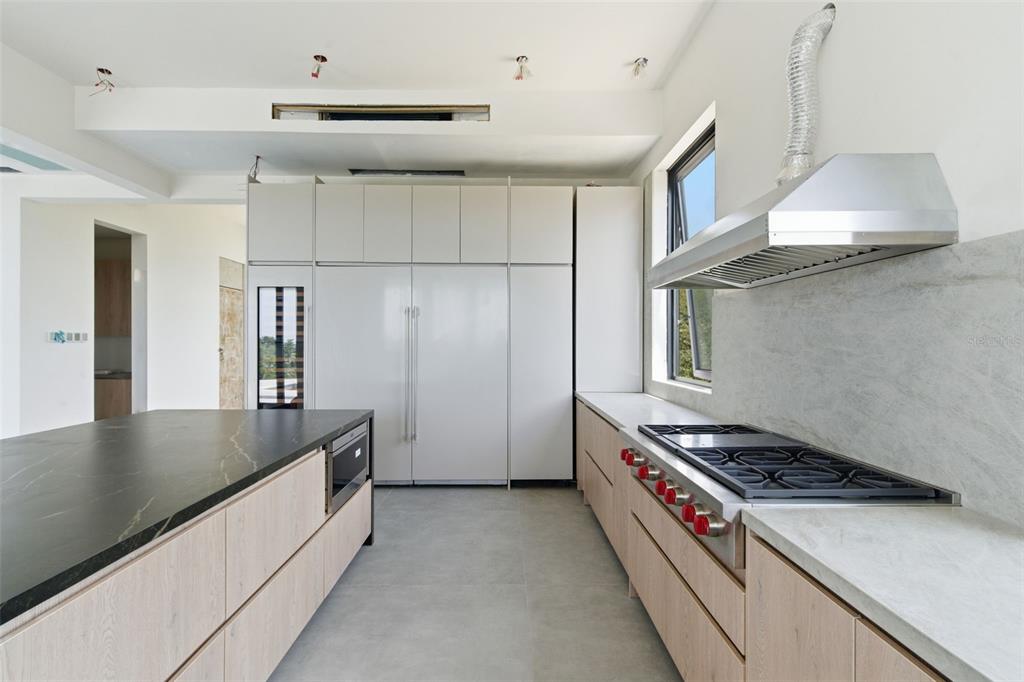 A modern kitchen features light wood cabinetry, a black stone island, and a stainless-steel range — 22 ROBLE VALLEY PALMAS DEL MAR, HUMACAO, PR