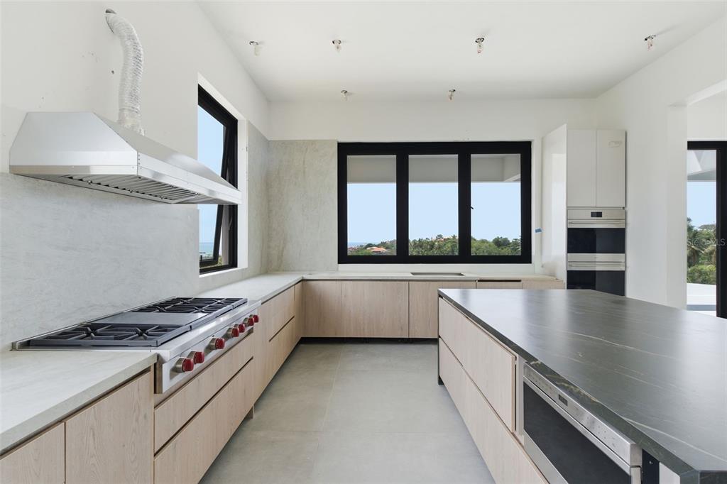 A modern kitchen features light wood cabinets, a dark stone island, and a large window — 22 ROBLE VALLEY PALMAS DEL MAR, HUMACAO, PR