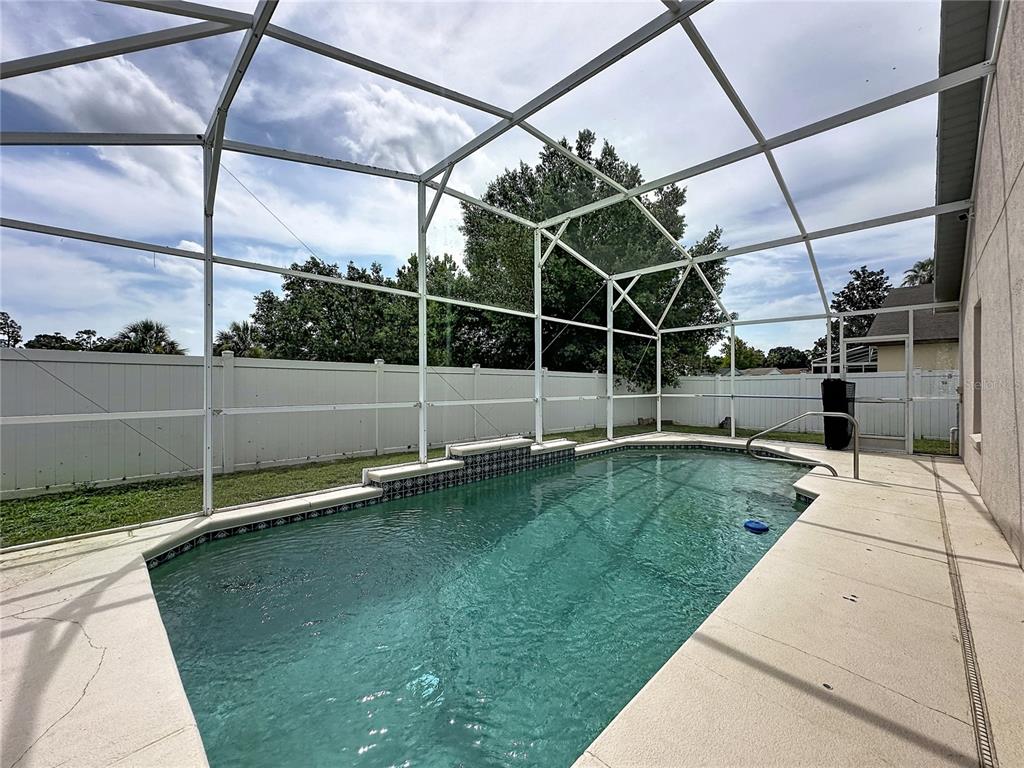 A swimming pool with a tiled water feature sits inside a screened-in patio enclosure — 659 DURANGO LOOP STREET, DAVENPORT, FL