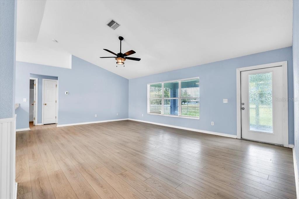 A spacious living room features light blue walls, wood-look flooring, a ceiling fan, and windows — 1708 BLUE LAKE CIRCLE, PUNTA GORDA, FL