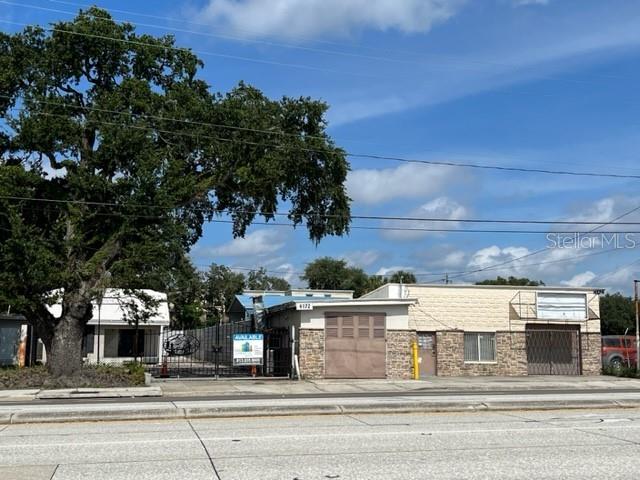 A commercial building with a stone facade and a large tree stands beside a road — 4172-4174 E HILLSBOROUGH AVENUE, TAMPA, FL