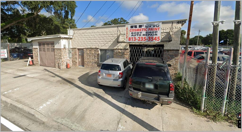 An exterior view of a single-story commercial auto body shop with a gravel parking lot — 4172-4174 E HILLSBOROUGH AVENUE, TAMPA, FL