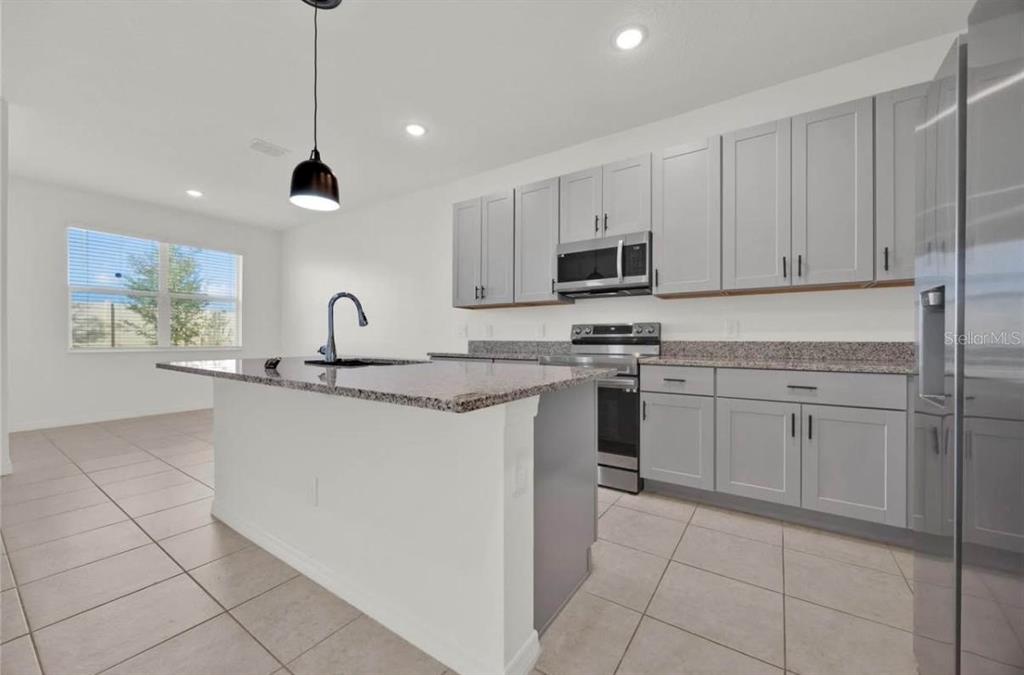 A kitchen features gray cabinets, granite countertops, a center island, and stainless steel appliances — 811 RICHMOND ESTATE AVENUE, HAINES CITY, FL