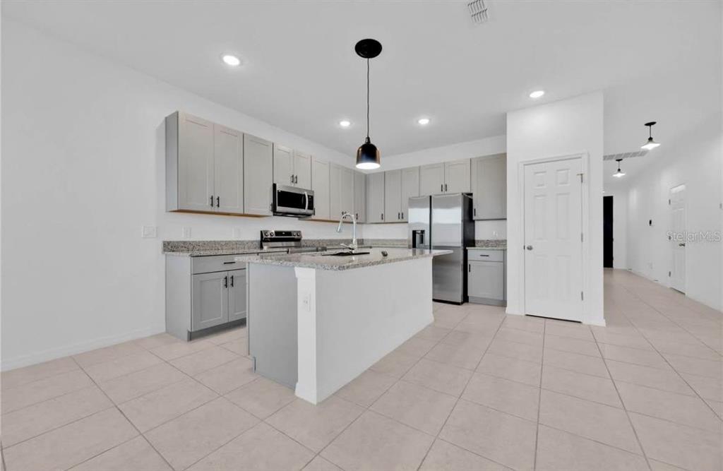 A kitchen features light gray cabinets, granite countertops, a center island, and stainless steel appliances — 811 RICHMOND ESTATE AVENUE, HAINES CITY, FL