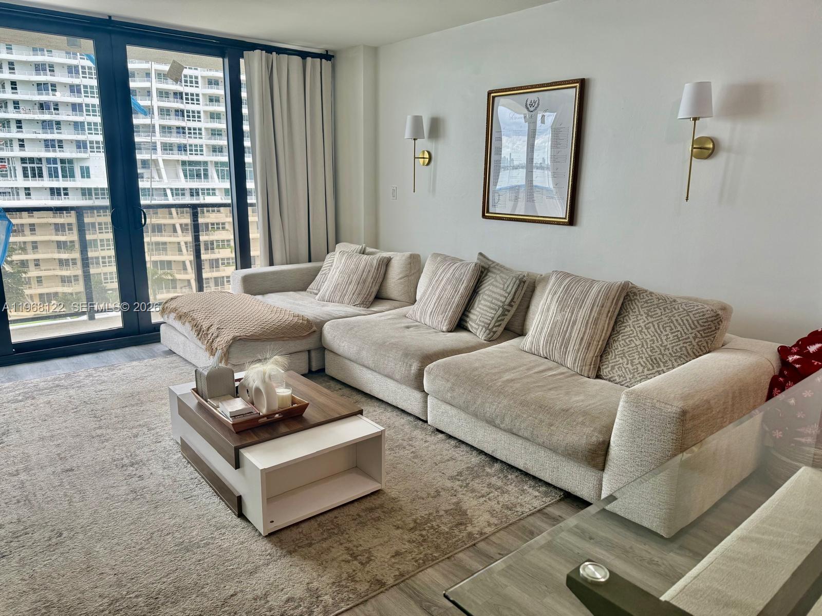 An empty room with wood-look flooring and floor-to-ceiling windows overlooking a bay and buildings — 600 NE 36th St # 820, Miami FL 33137, MIAMI, FL