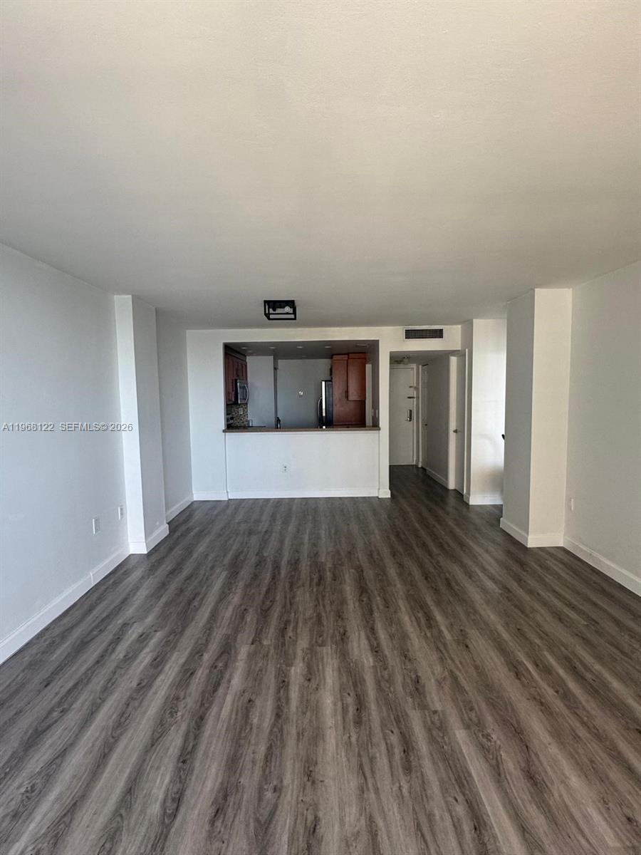An empty living area features gray wood-look flooring and an open pass-through to the kitchen — 600 NE 36th St # 820, Miami FL 33137, MIAMI, FL