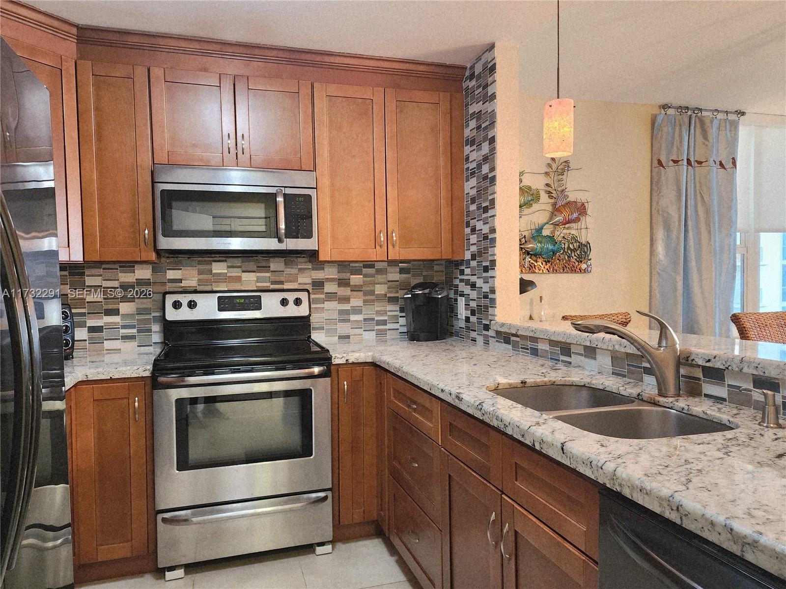 A kitchen features wood cabinets, stainless steel appliances, granite countertops, and a mosaic tile backsplash — 3505 S Ocean Dr # 1206, Hollywood FL 33019, HOLLYWOOD, FL