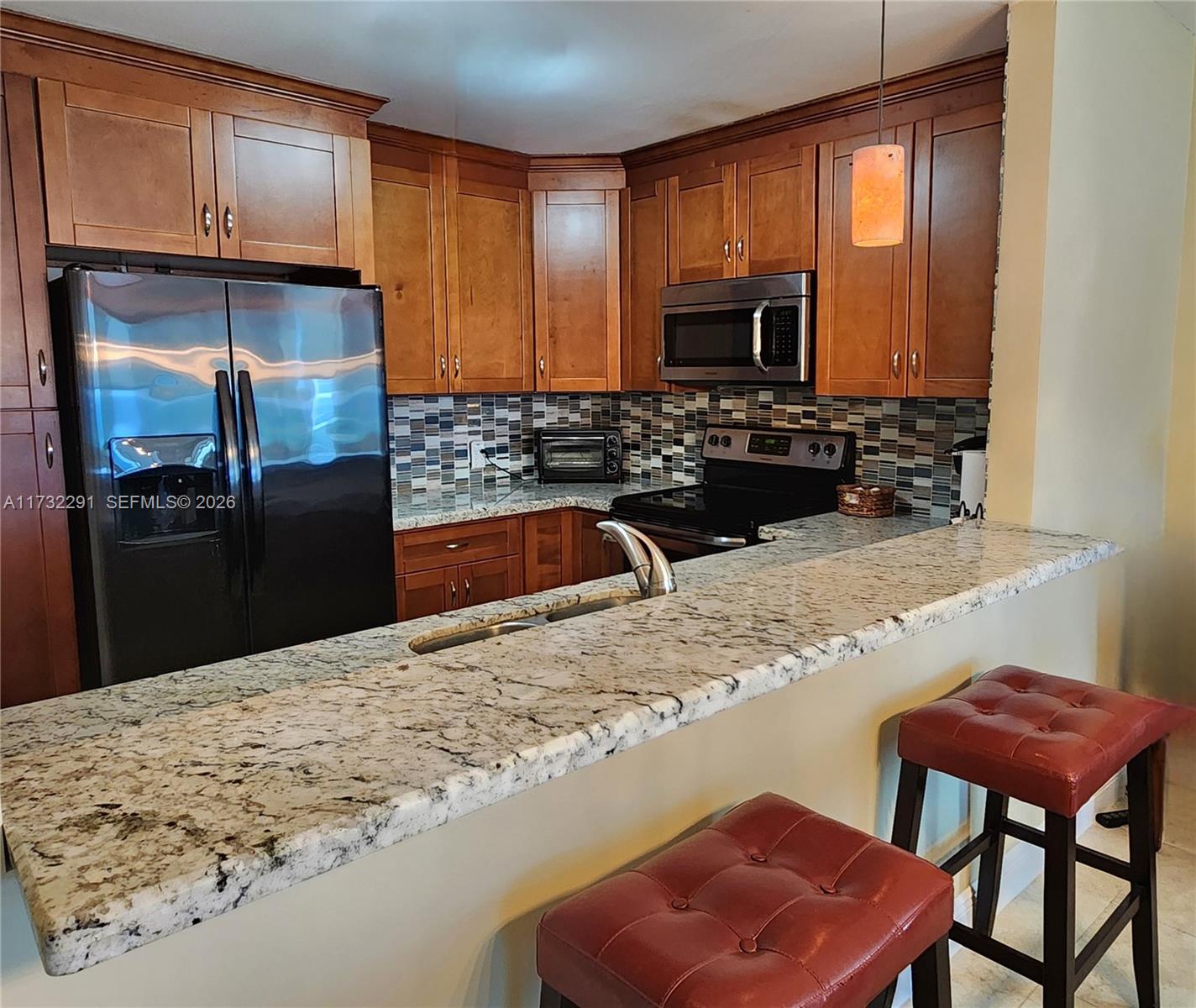 A kitchen features wood cabinets, granite countertops, a breakfast bar, and a mosaic tile backsplash — 3505 S Ocean Dr # 1206, Hollywood FL 33019, HOLLYWOOD, FL