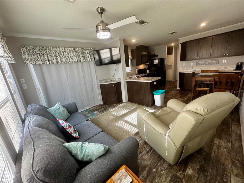 An open-concept living room and kitchen featuring dark cabinetry, wood-look flooring, and a ceiling fan — 14365 NE 252ND COURT ROAD UNIT 123, SALT SPRINGS, FL