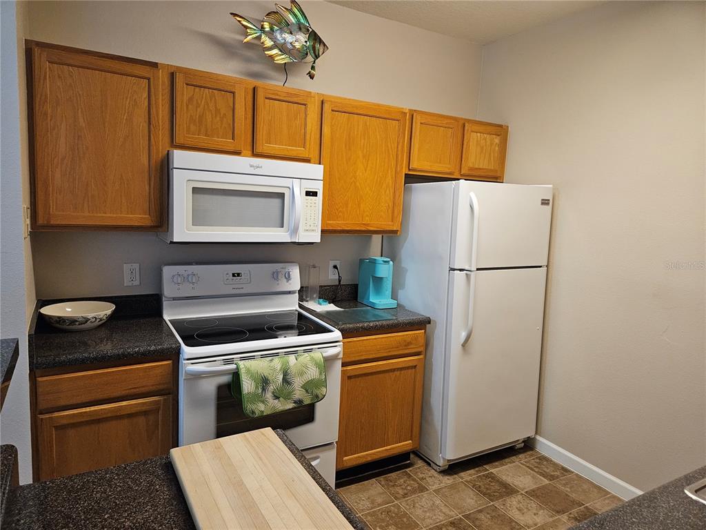 A kitchen features oak cabinets, dark countertops, white appliances, and a tiled floor — 4802 51ST STREET W UNIT 1417, BRADENTON, FL