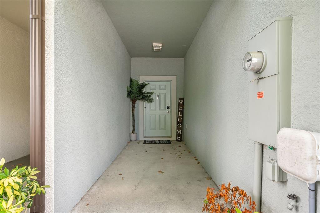 A covered entryway features a light-colored door, a welcome sign, and an exterior utility meter — 7627 FRENCH MARIGOLD AVENUE, TAMPA, FL