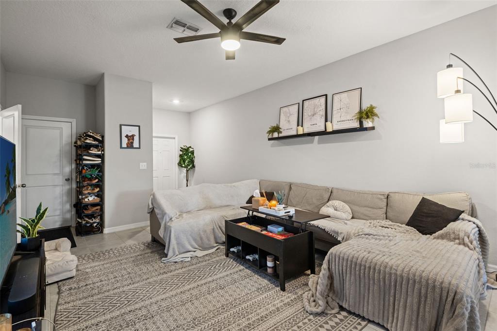 A living room features a sectional sofa, a lift-top coffee table, and a wall-mounted shelf — 7627 FRENCH MARIGOLD AVENUE, TAMPA, FL