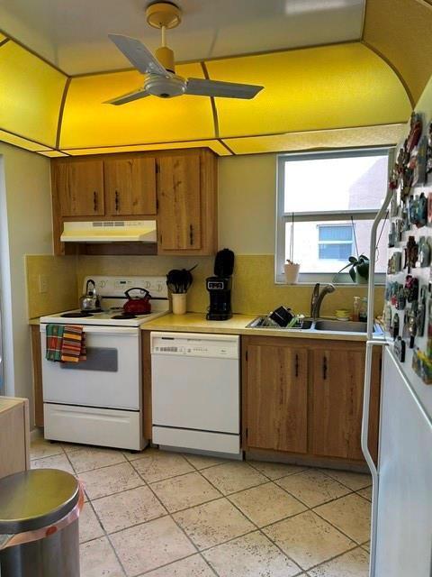 A kitchen features wood cabinets, a white stove and dishwasher, and a yellow ceiling light — 6770 Royal Palm Boulevard # 301, Margate FL 33063, MARGATE, FL