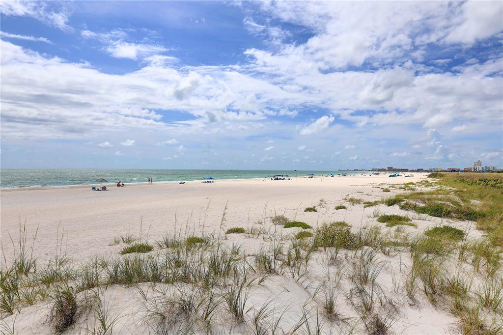 A wide, sandy beach with dune grass in the foreground under a cloudy blue sky — 9980 GULF BOULEVARD UNIT 522, TREASURE ISLAND, FL