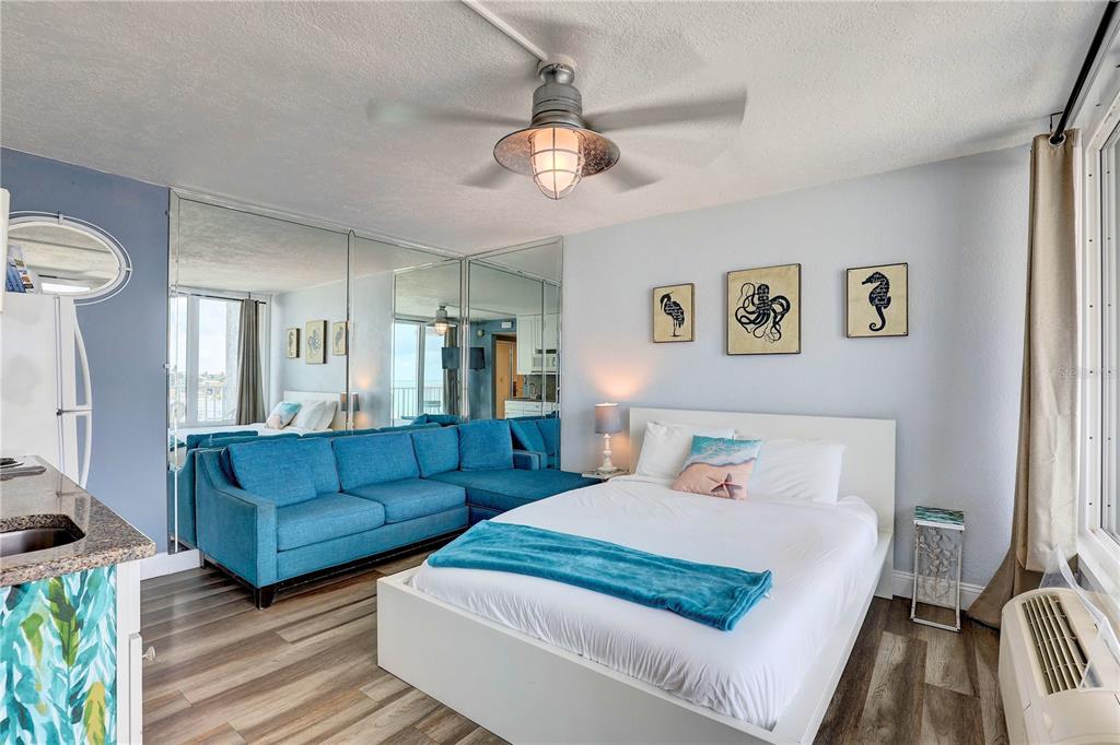 A studio apartment features a bed, blue sectional sofa, mirrored wall, and a ceiling fan — 9980 GULF BOULEVARD UNIT 522, TREASURE ISLAND, FL
