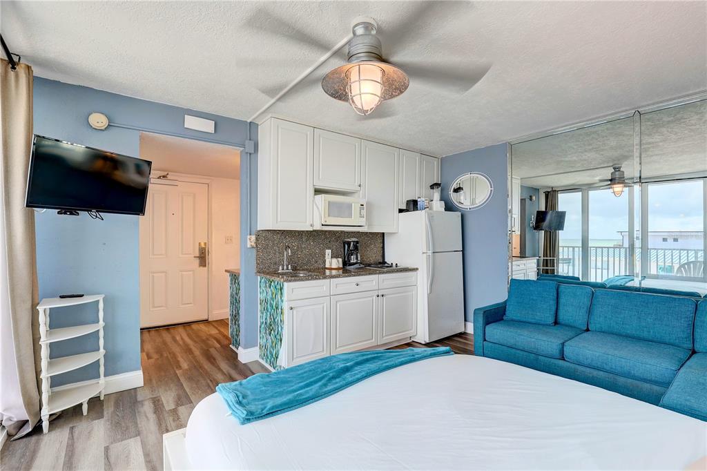 A studio apartment features a kitchenette, a blue sofa, a bed, and a mirrored wall — 9980 GULF BOULEVARD UNIT 522, TREASURE ISLAND, FL