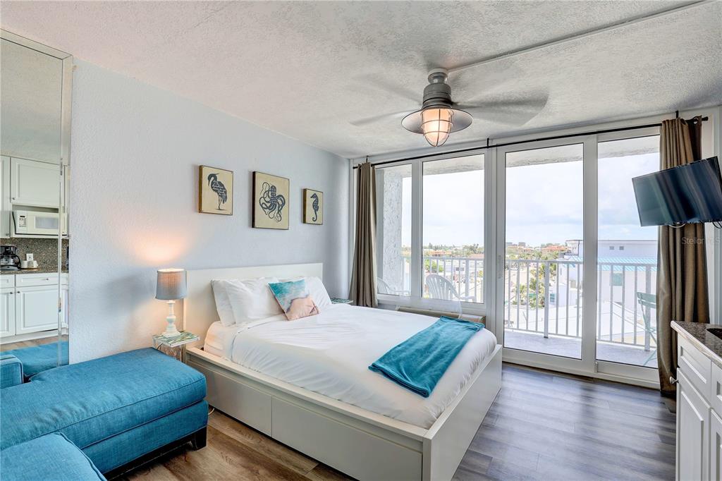 A bedroom features a white platform bed, blue accent furniture, and a balcony with views — 9980 GULF BOULEVARD UNIT 522, TREASURE ISLAND, FL
