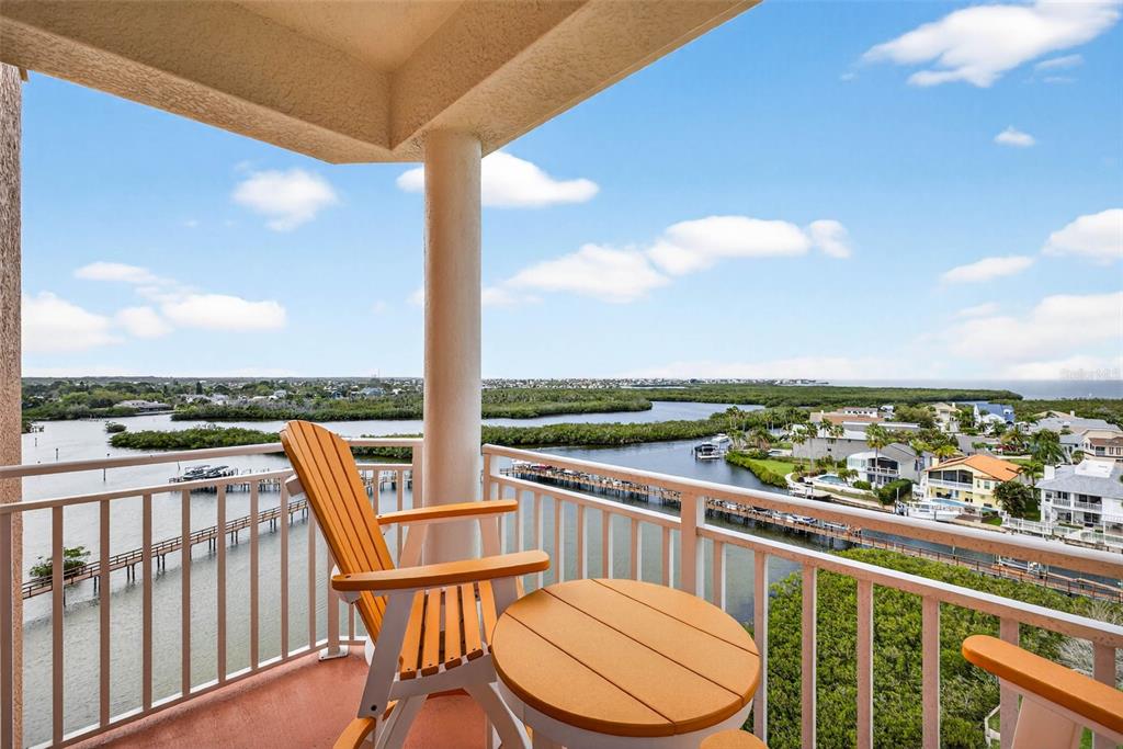 A balcony with a table and chair overlooks a waterway, mangroves, and coastal houses — 4516 SEAGULL DRIVE UNIT 902, NEW PORT RICHEY, FL