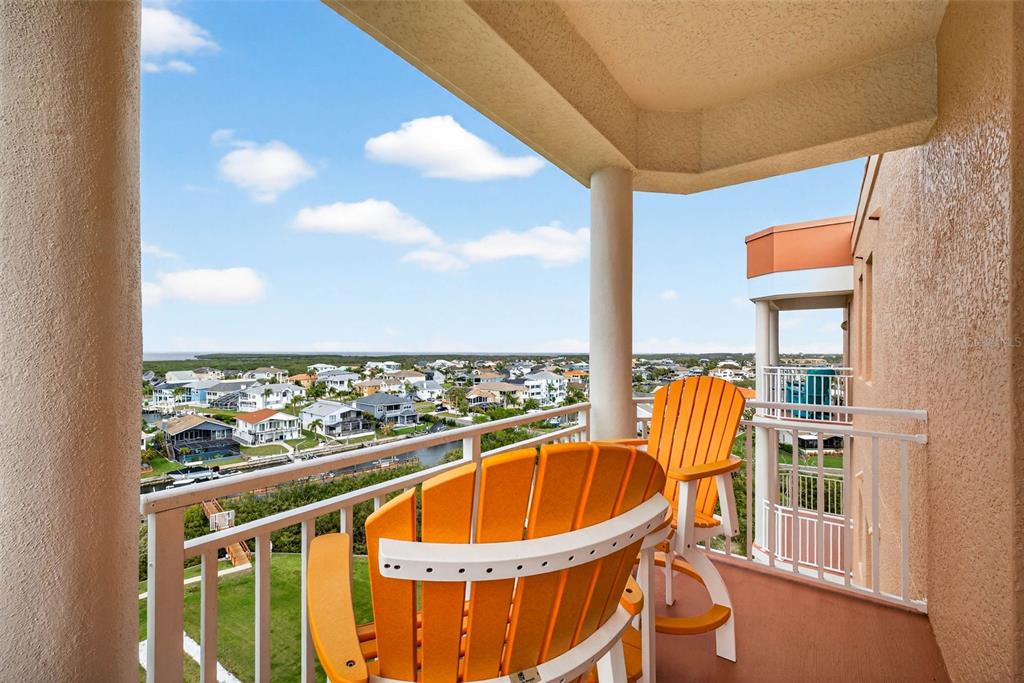 A balcony with two orange chairs overlooks a residential neighborhood and a distant body of water — 4516 SEAGULL DRIVE UNIT 902, NEW PORT RICHEY, FL