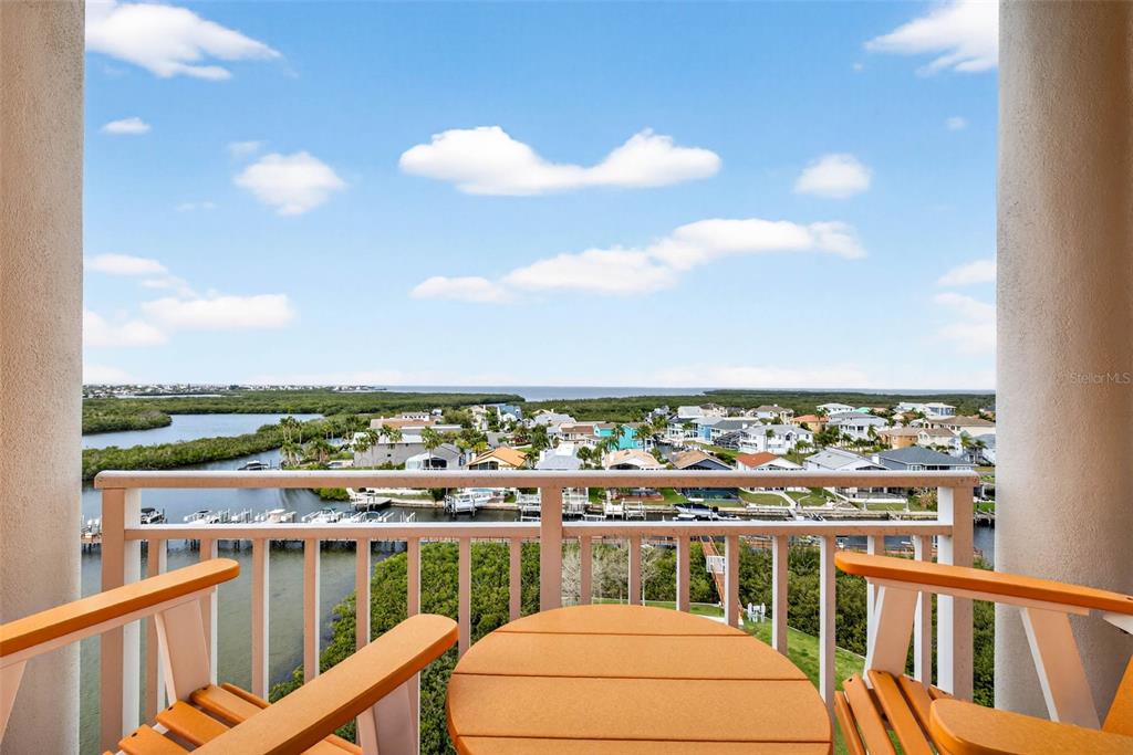 A balcony with two orange chairs and a table overlooks a coastal residential area — 4516 SEAGULL DRIVE UNIT 902, NEW PORT RICHEY, FL