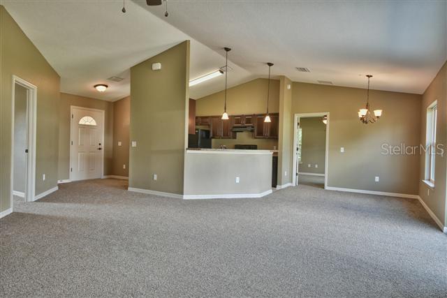 A living room with carpeted floors leads to an open kitchen with a breakfast bar — 12177 SW 96TH LANE, DUNNELLON, FL