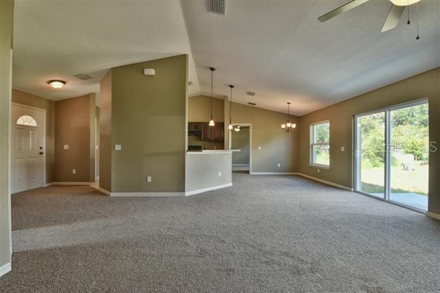 An open-concept living area features beige carpet, tan walls, a kitchen island, and sliding glass doors — 12177 SW 96TH LANE, DUNNELLON, FL