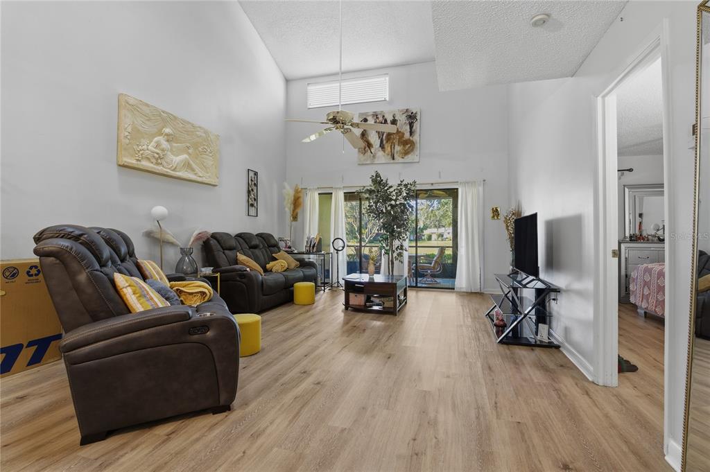 A living room with high ceilings, wood-look flooring, dark leather seating, and sliding glass doors — 116 COVENTRY LN, HAINES CITY, FL