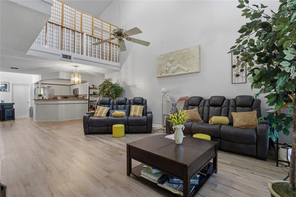 A living room with high ceilings, a loft balcony, two dark sofas, and wood-look flooring — 116 COVENTRY LN, HAINES CITY, FL
