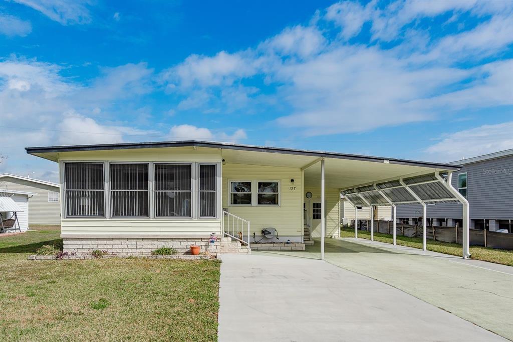 A light yellow manufactured home with a screened-in porch and an attached carport — 127 INDEPENDENCE AVENUE, PALM HARBOR, FL