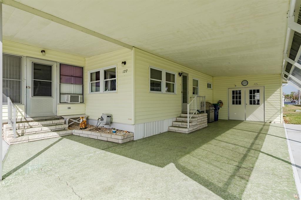 A yellow mobile home features a large covered carport, two entryways, and stone-accented steps — 127 INDEPENDENCE AVENUE, PALM HARBOR, FL