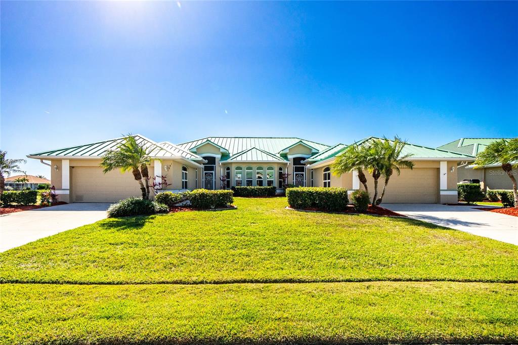 A wide, single-story house with a green metal roof and two attached garages — 1551 ATARES DRIVE UNIT 112, PUNTA GORDA, FL