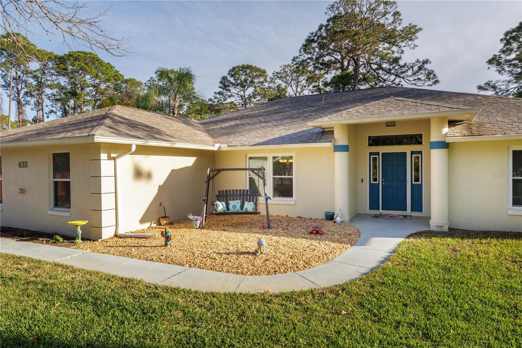 A single-story house with a beige exterior, a blue front door, and a gravel front yard — 633 ART CENTER AVENUE, NEW SMYRNA BEACH, FL