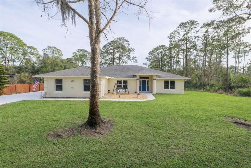 A single-story house with a light-colored exterior sits on a large, grassy lot — 633 ART CENTER AVENUE, NEW SMYRNA BEACH, FL