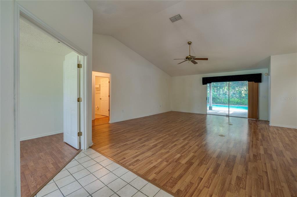 An empty living room features wood-look flooring, a vaulted ceiling, and sliding glass patio doors — 203 LIVE OAK COURT, LAKE MARY, FL