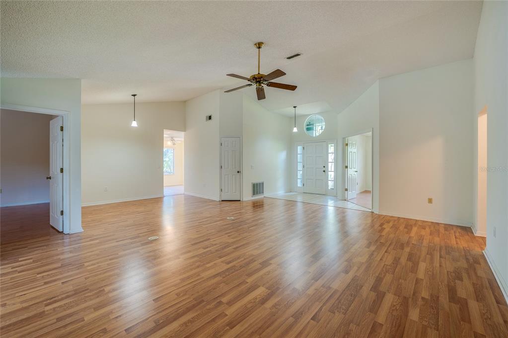 A spacious living area with light wood-look flooring, a vaulted ceiling, and a ceiling fan — 203 LIVE OAK COURT, LAKE MARY, FL