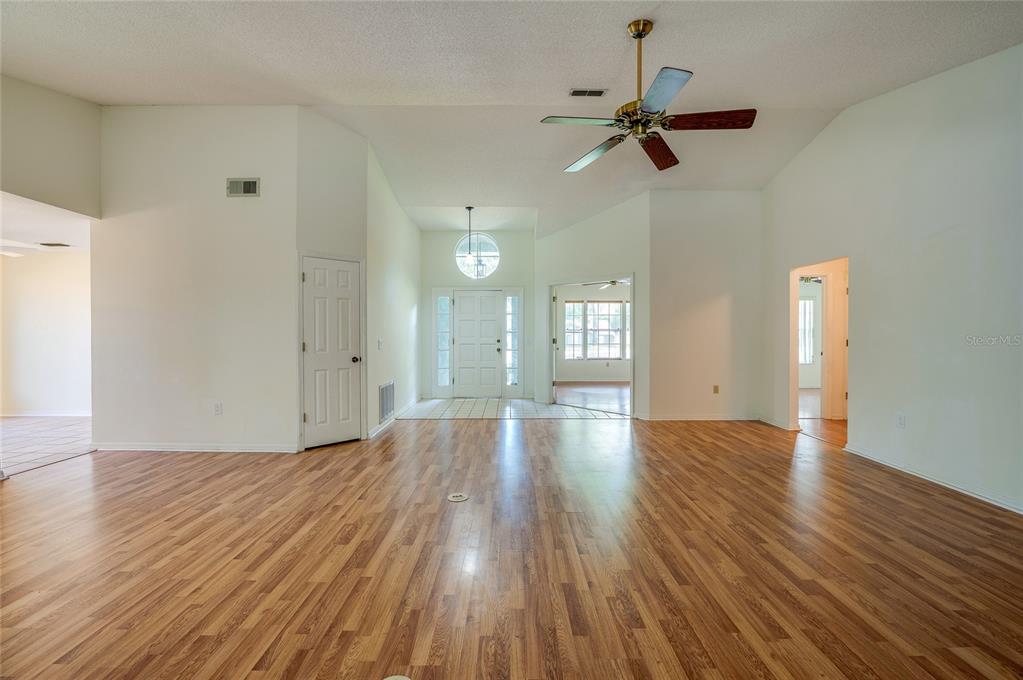 A spacious living room features wood-look flooring, a vaulted ceiling with a fan, and an entryway — 203 LIVE OAK COURT, LAKE MARY, FL