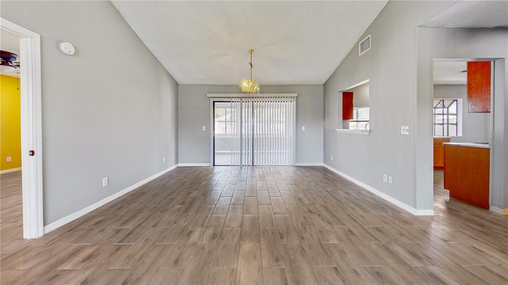 A living room with wood-look tile flooring, a vaulted ceiling, and a sliding glass door — 305 MEDINA COURT, KISSIMMEE, FL